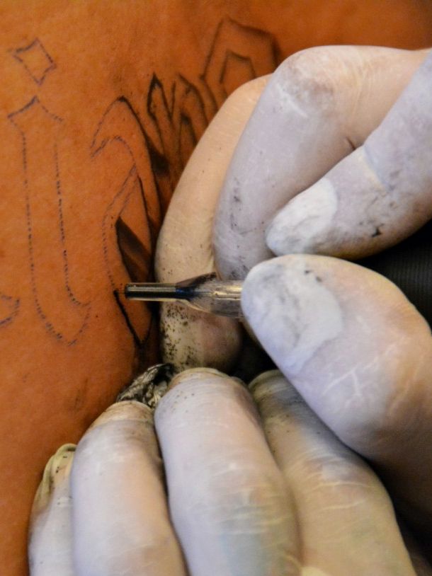 Artist pulling the outline of a lettering tattoo