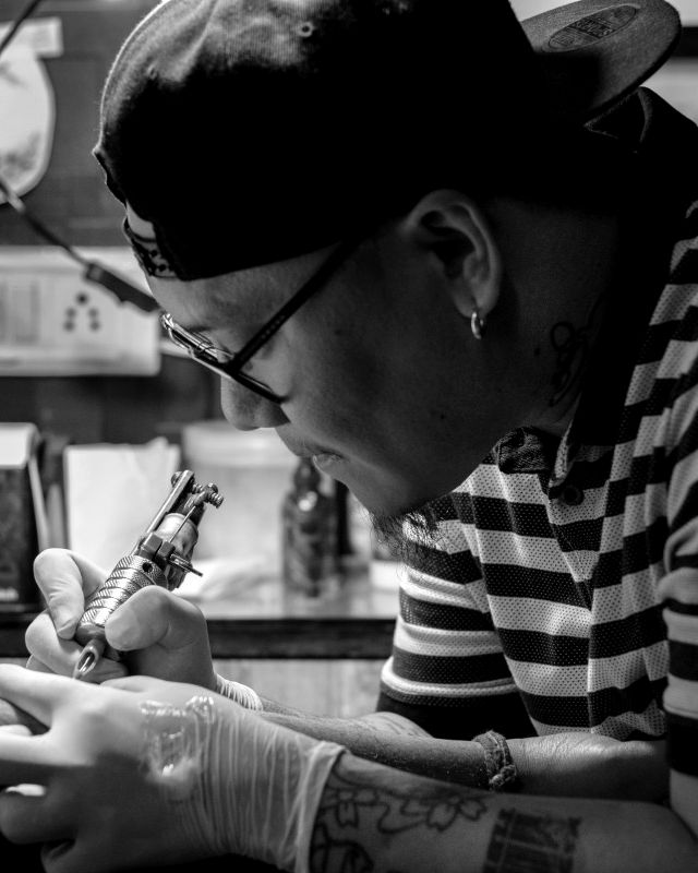 Nova Kerr tattooing a client’s hand, black and white